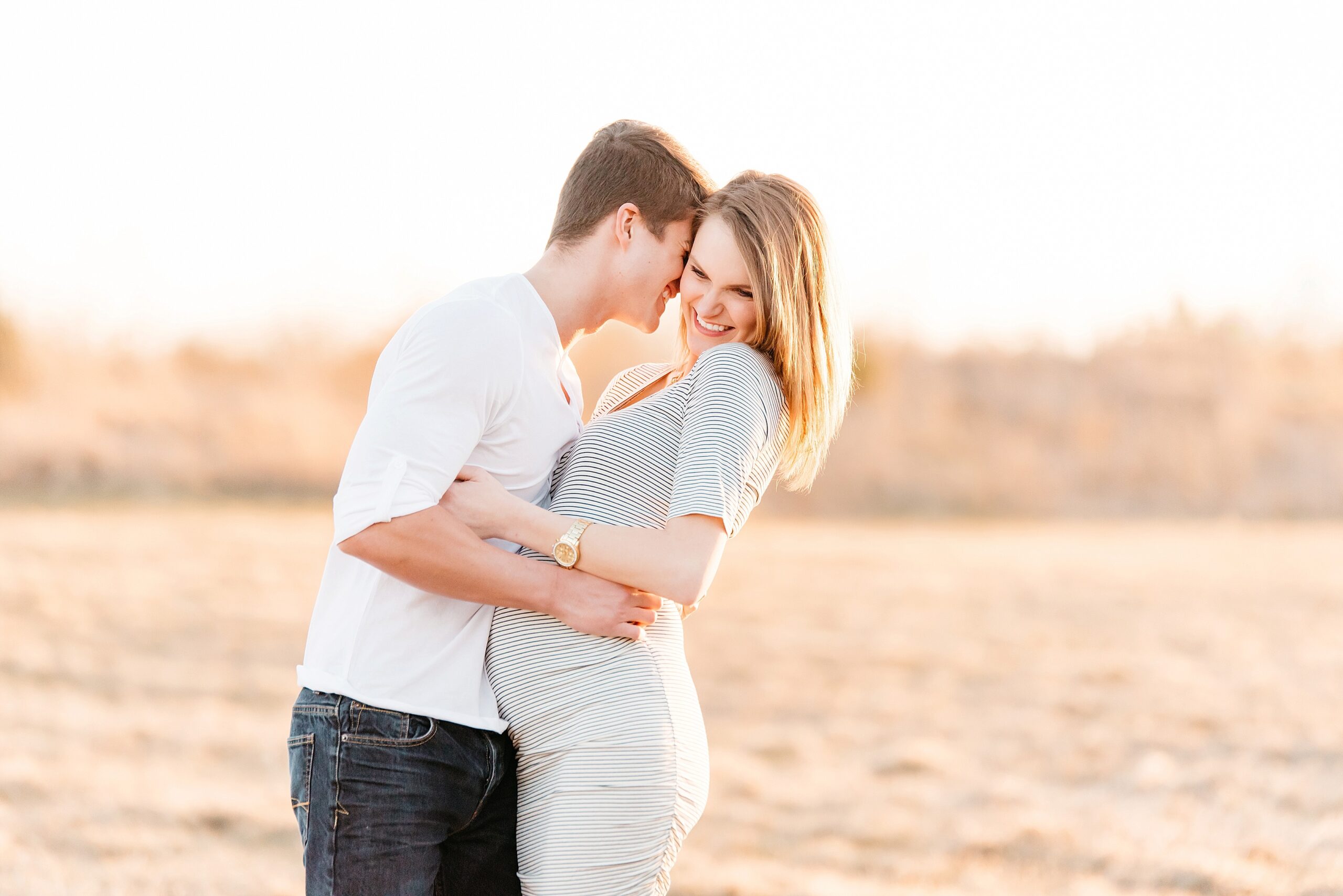 golden hour maternity photo of couple nuzzling and laughing